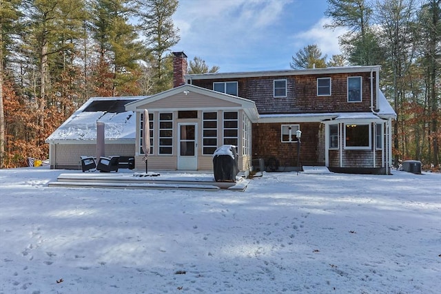 snow covered house with central AC unit and a sunroom