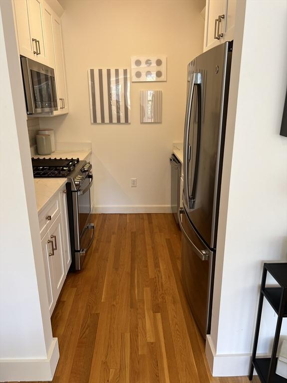 90 Broadway Unit 2C, Boston, MA 02116 - kitchen with stainless steel appliances, wood finished floors, white cabinetry, and light countertops