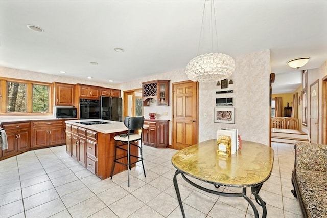 kitchen featuring brown cabinetry, a kitchen island, black appliances, light tile patterned floors, and a notable chandelier