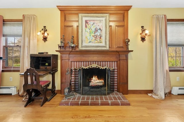 sitting room with baseboards, a baseboard radiator, a brick fireplace, and wood finished floors