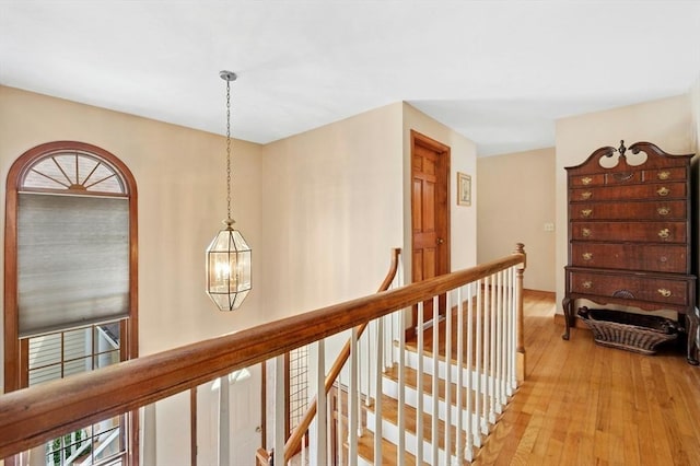 hall featuring light wood-style flooring, a chandelier, and an upstairs landing