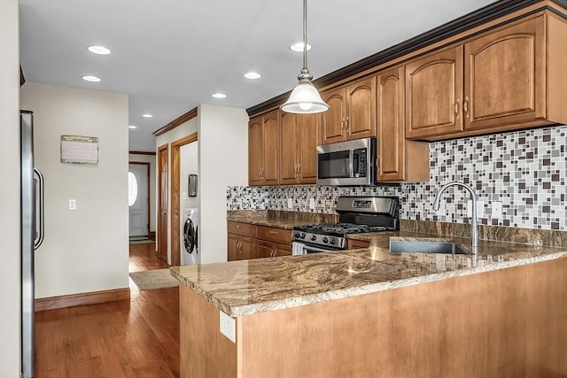 kitchen featuring washer / dryer, appliances with stainless steel finishes, kitchen peninsula, and dark stone counters