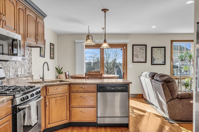 kitchen featuring decorative light fixtures, sink, decorative backsplash, stainless steel appliances, and light hardwood / wood-style flooring