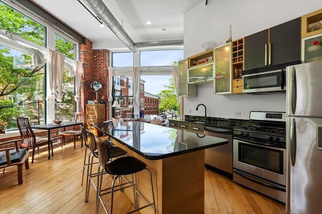 281 Essex St Unit 206, Salem, MA 01970 - kitchen with appliances with stainless steel finishes, light wood-style flooring, a kitchen breakfast bar, a center island, and glass insert cabinets