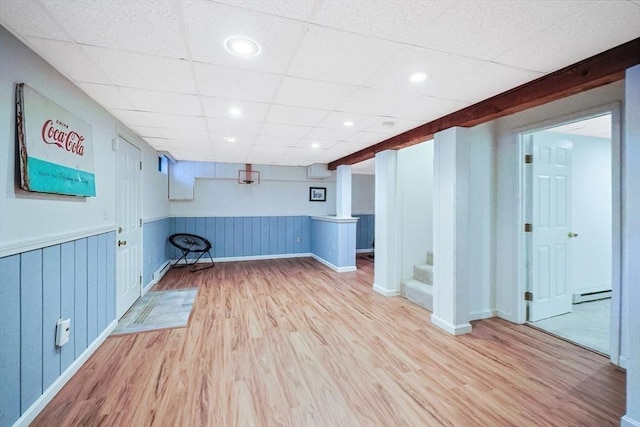 finished below grade area featuring a drop ceiling, stairs, baseboard heating, wainscoting, and wood finished floors