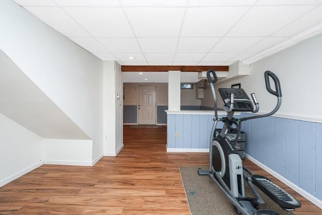 exercise room with a wainscoted wall, a paneled ceiling, and light wood-type flooring