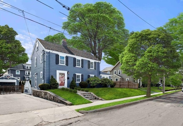 colonial-style house featuring fence, a chimney, and a front lawn