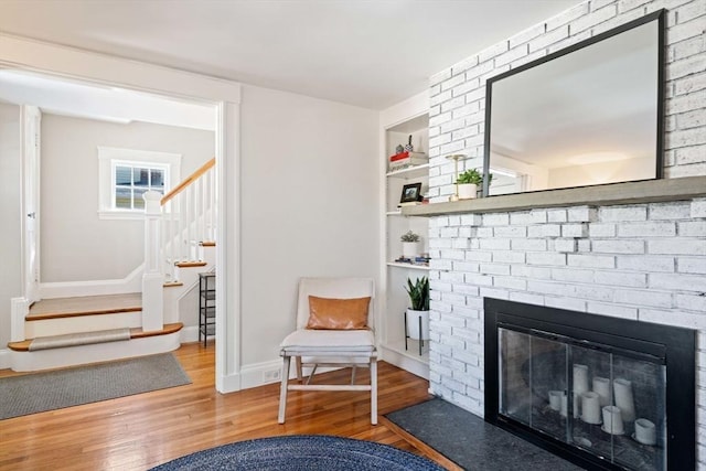 sitting room with built in shelves, a fireplace, wood finished floors, baseboards, and stairs