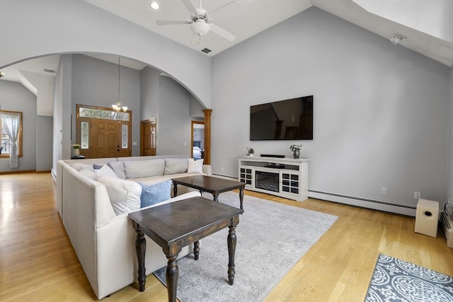 living area with arched walkways, light wood-style flooring, a baseboard radiator, high vaulted ceiling, and a ceiling fan