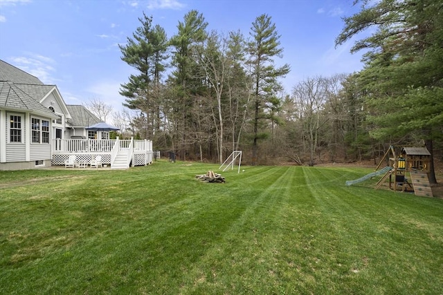 view of yard featuring a wooden deck, a playground, and an outdoor fire pit