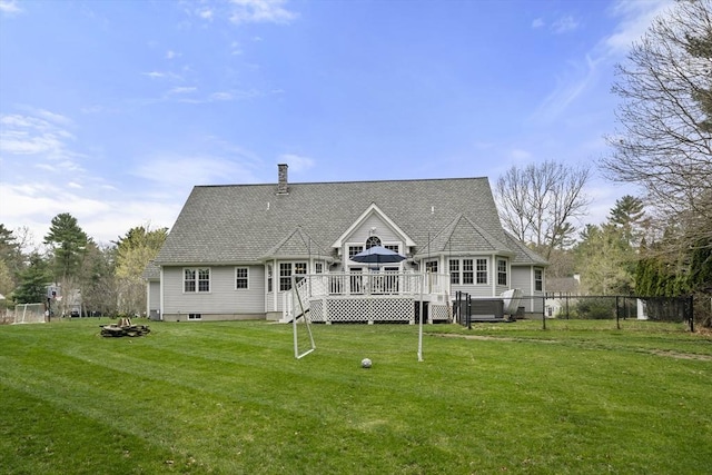 back of property featuring a deck, an outdoor fire pit, fence, roof with shingles, and a lawn