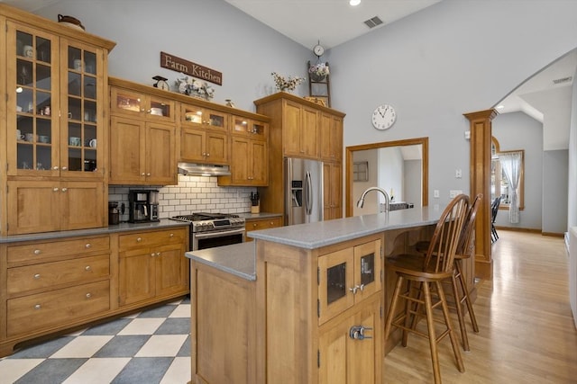 kitchen featuring tasteful backsplash, decorative columns, stainless steel appliances, under cabinet range hood, and visible vents