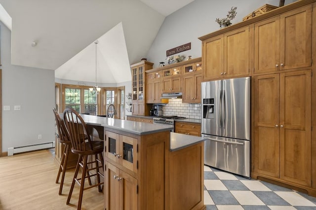 kitchen featuring stainless steel appliances, a baseboard heating unit, under cabinet range hood, light floors, and brown cabinetry