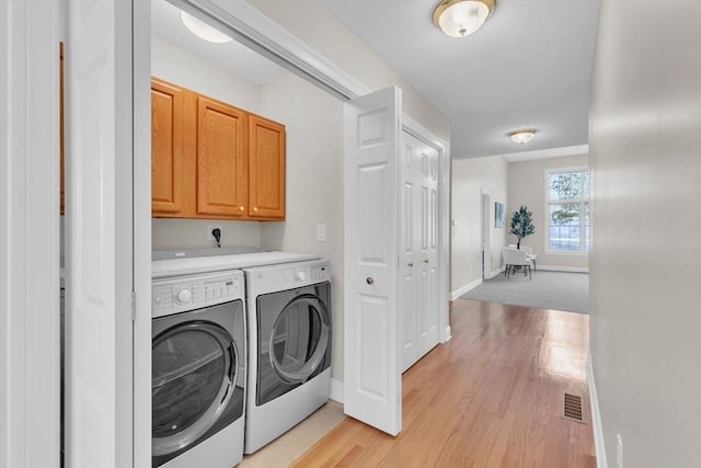 clothes washing area with washing machine and dryer, cabinets, and light wood-type flooring