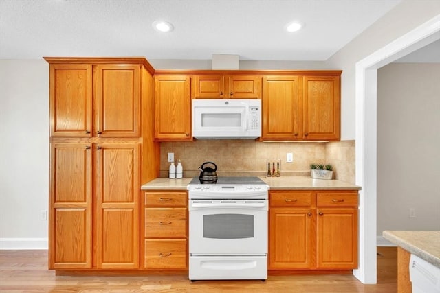 kitchen with tasteful backsplash, white appliances, and light hardwood / wood-style flooring