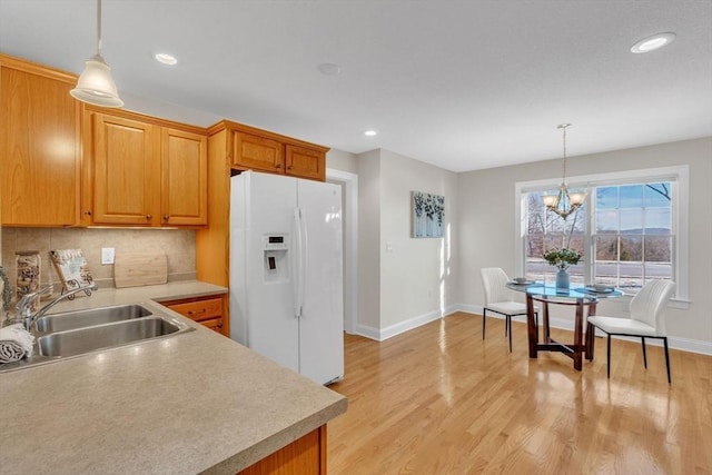 kitchen featuring hanging light fixtures, sink, backsplash, and white refrigerator with ice dispenser