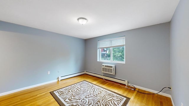 spare room with baseboard heating, a wall mounted air conditioner, wood finished floors, and baseboards