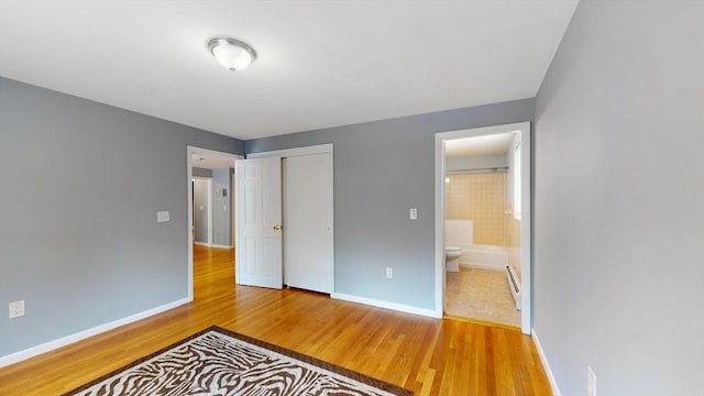 bedroom featuring a closet, baseboard heating, wood finished floors, and baseboards