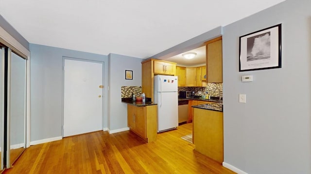 kitchen with tasteful backsplash, dark countertops, freestanding refrigerator, light wood-type flooring, and dishwasher