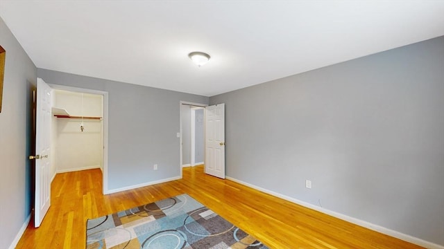 unfurnished bedroom with a spacious closet, a closet, baseboards, and wood finished floors