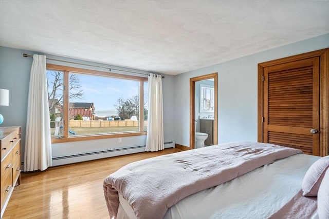 bedroom featuring light wood-style flooring, ensuite bath, and a baseboard heating unit