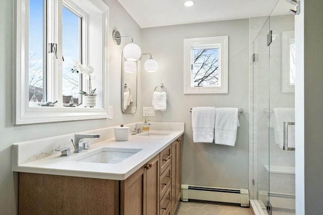 full bath with a sink, a baseboard heating unit, a stall shower, and double vanity