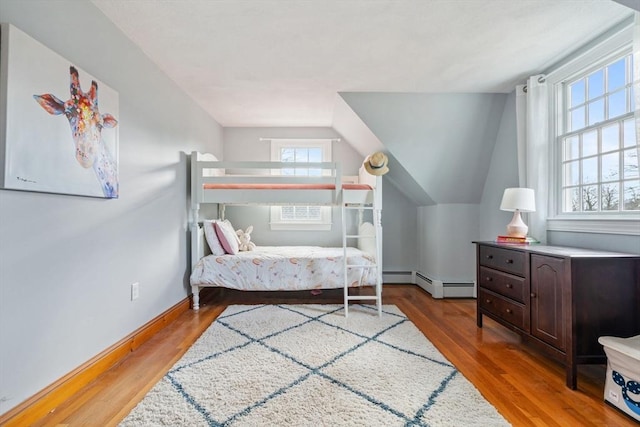 bedroom with multiple windows, wood finished floors, baseboards, and baseboard heating