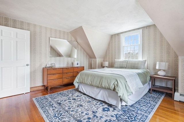 bedroom featuring baseboards, wood-type flooring, lofted ceiling, and wallpapered walls