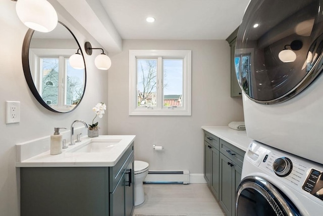 bathroom with stacked washer / drying machine, plenty of natural light, baseboard heating, and toilet