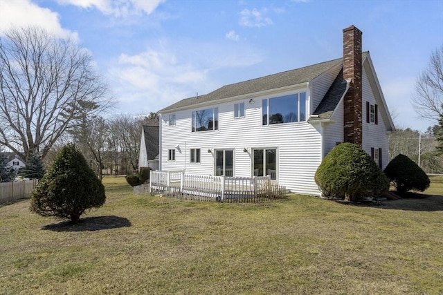 rear view of house featuring a lawn, a deck, fence, roof with shingles, and a chimney