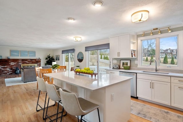 kitchen featuring a sink, stainless steel dishwasher, a breakfast bar area, white cabinets, and light wood finished floors