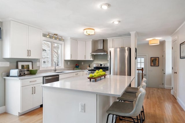 kitchen with a sink, appliances with stainless steel finishes, a kitchen bar, wall chimney exhaust hood, and a center island