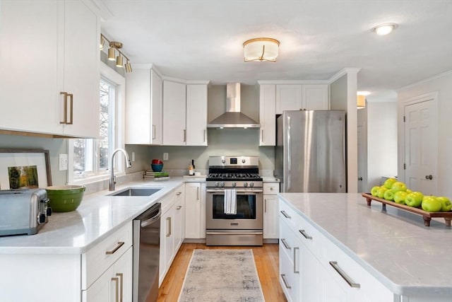 kitchen featuring light wood finished floors, wall chimney range hood, white cabinets, stainless steel appliances, and a sink