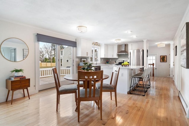 dining space with a baseboard heating unit, light wood-style flooring, and ornamental molding