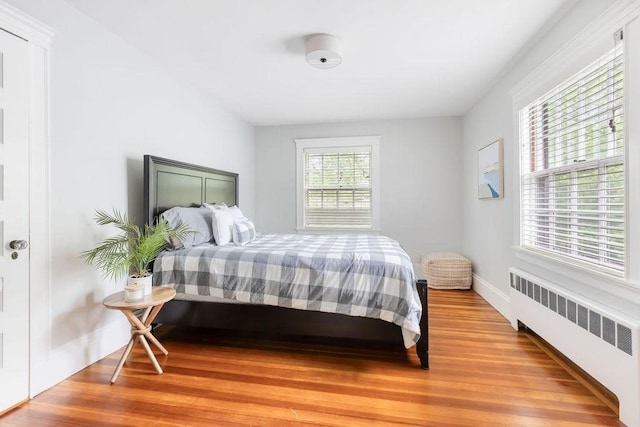 bedroom featuring light wood finished floors, baseboards, and radiator heating unit