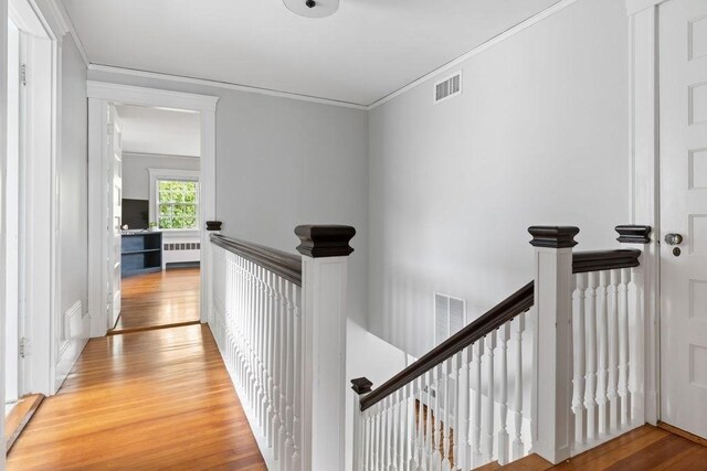 hall with radiator, light wood-type flooring, an upstairs landing, and visible vents