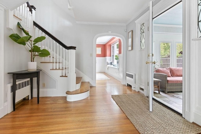 foyer with arched walkways, radiator heating unit, light wood-type flooring, and plenty of natural light