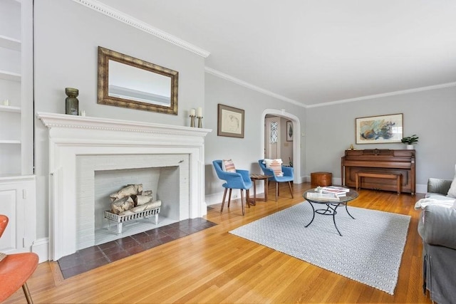 living room with arched walkways, a fireplace with flush hearth, crown molding, and wood finished floors
