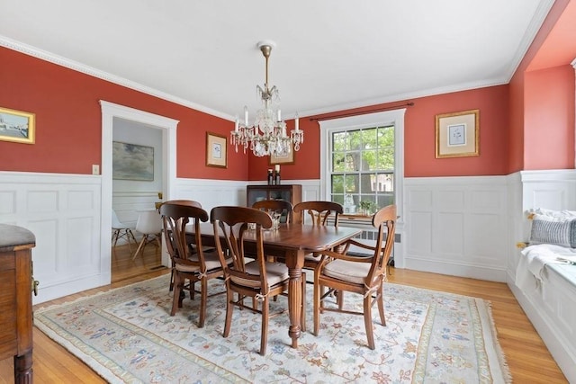 dining area with ornamental molding, a chandelier, light wood-type flooring, and wainscoting