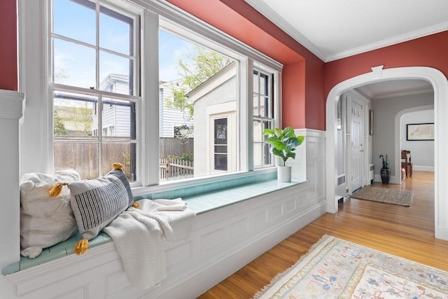 hall featuring ornamental molding, a wealth of natural light, arched walkways, and light wood-style floors
