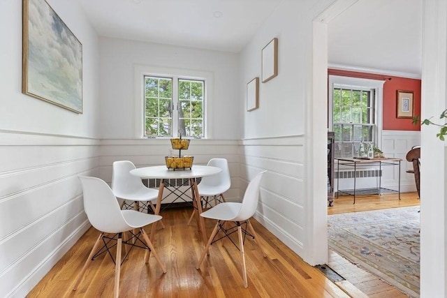 dining space with wainscoting, a decorative wall, and wood finished floors