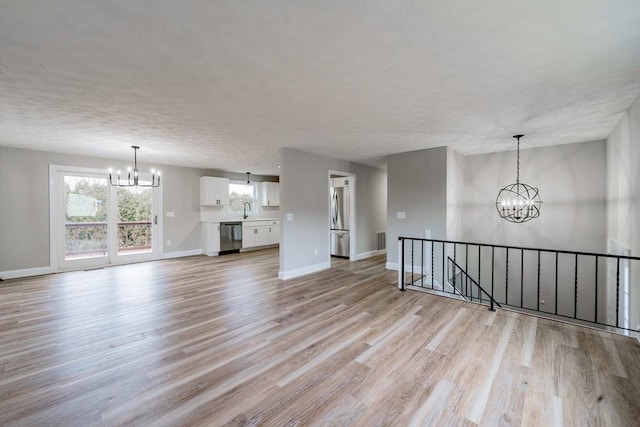 unfurnished living room with light hardwood / wood-style floors, sink, and a notable chandelier