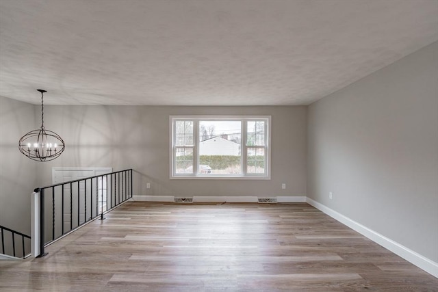 spare room with light wood-type flooring and a chandelier