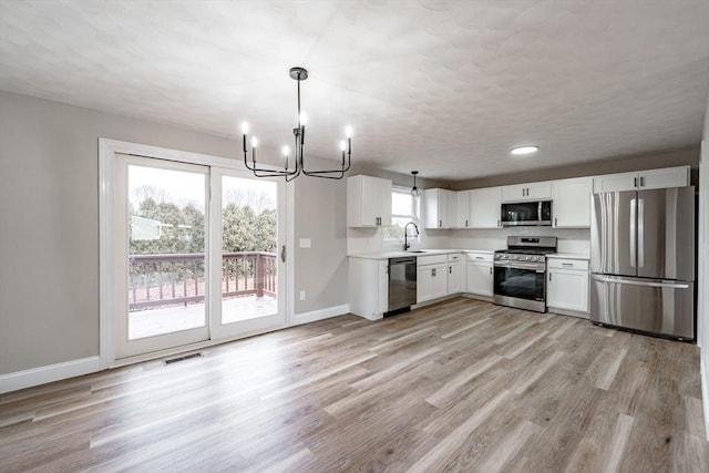 kitchen featuring white cabinetry, stainless steel appliances, sink, hanging light fixtures, and light hardwood / wood-style flooring