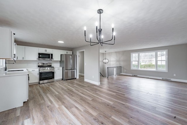 kitchen featuring white cabinetry, appliances with stainless steel finishes, hanging light fixtures, a chandelier, and sink