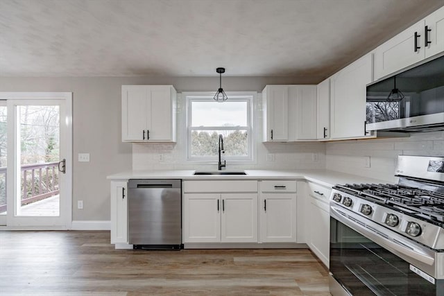 kitchen with a wealth of natural light, white cabinets, appliances with stainless steel finishes, sink, and hanging light fixtures