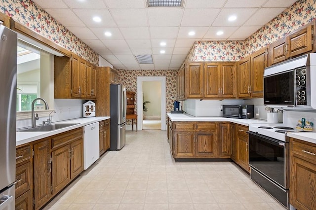 127 E St, East Bridgewater, MA 02333 - kitchen with stainless steel appliances, wallpapered walls, a sink, light countertops, and brown cabinetry