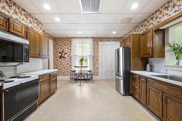 127 E St, East Bridgewater, MA 02333 - kitchen with stainless steel appliances, wallpapered walls, a sink, light countertops, and brown cabinets