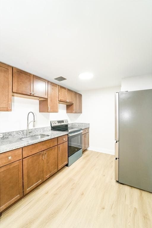 80 Main St Unit 4, Malden, MA 02148 - kitchen with stainless steel appliances, a sink, light wood-type flooring, brown cabinets, and light stone countertops