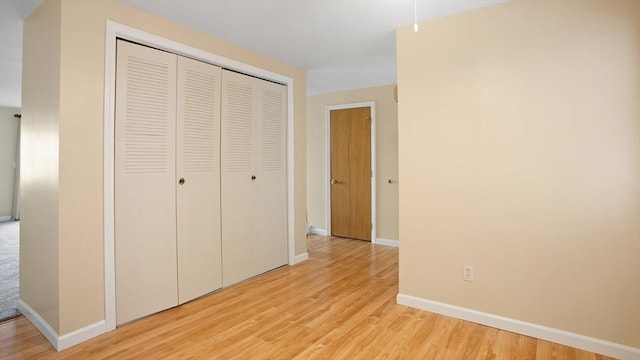 unfurnished bedroom featuring a closet, light wood-type flooring, and baseboards